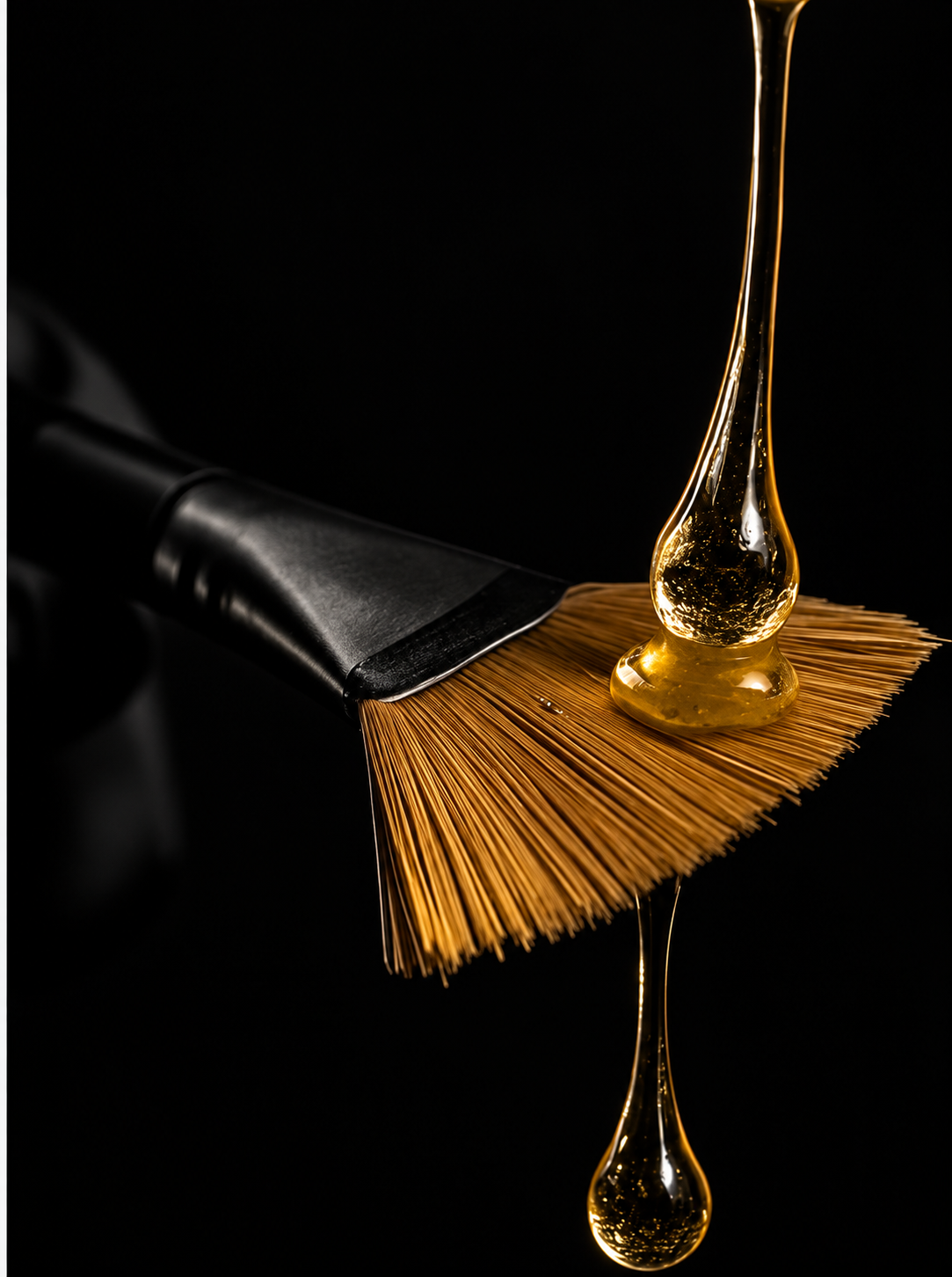 Golden liquid falling onto a salon color brush against a deep black background